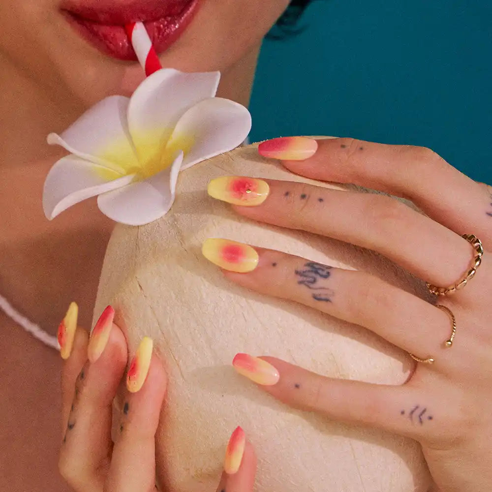 Sarı ve pembe ombre tırnaklara sahip eller, bir içecekli hindistan cevizini tutuyor, yanındaki plumeria çiçeğiyle birlikte.