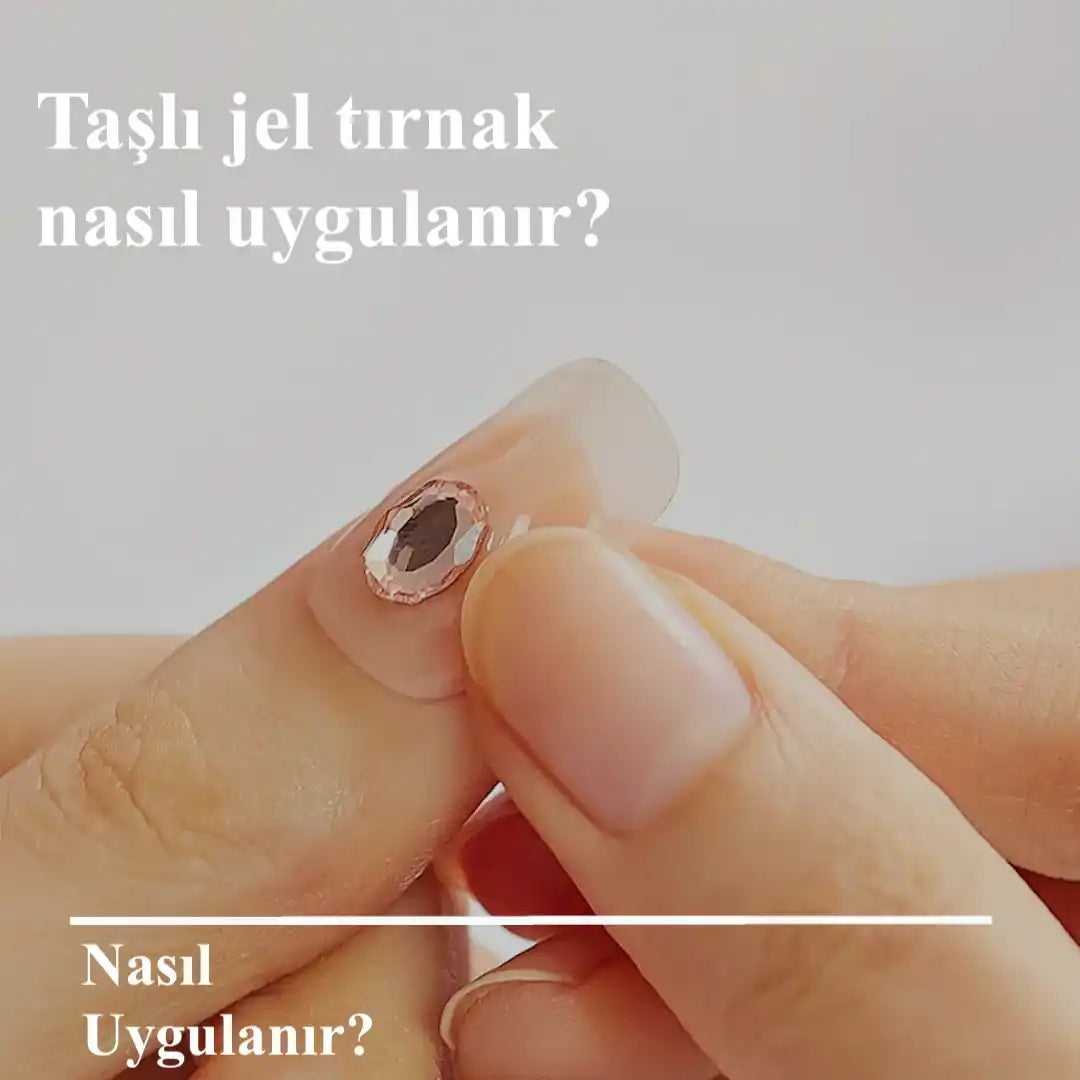 Bir kadın elinde, tırnak kenarına yakın bir yerde yapay, şeffaf, badem şeklinde bir tırnak ve üzerinde tek, oval pembe renkte bir rhinestone tutuyor.